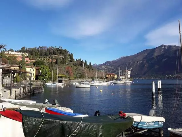 Uisce réidh dorcha gorm, luaimh bhána sneachta, sléibhte ollmhóra - Tírdhreacha súl spreagúla agus an áilleacht seo go léir ar Loch Como san Iodáil